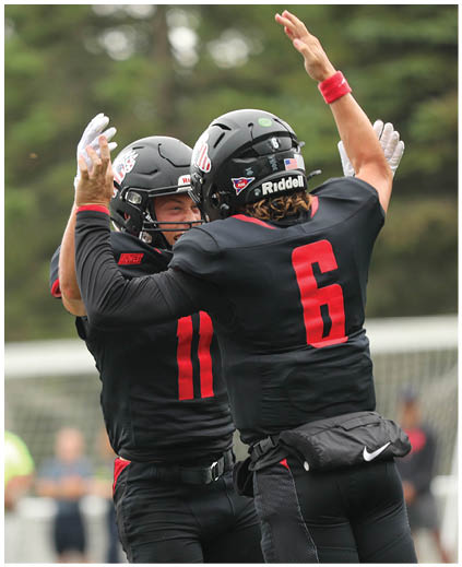 Two men wearing black jerseys with red numbers on them celebrating. Description generated by AI