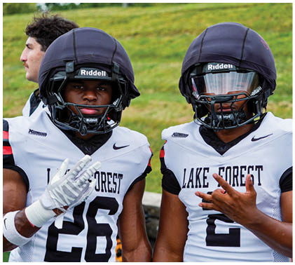 Two football players wearing helmets and jerseys. Description generated by AI