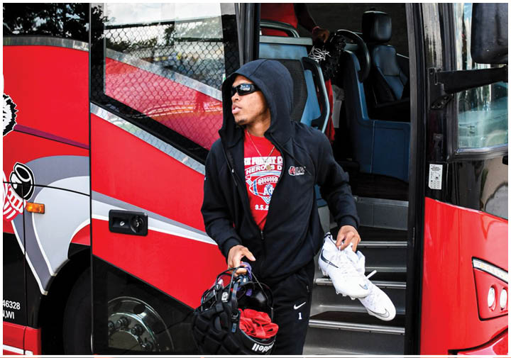 A man wearing a black hoodie and white shoes is walking towards a red bus. Description generated by AI