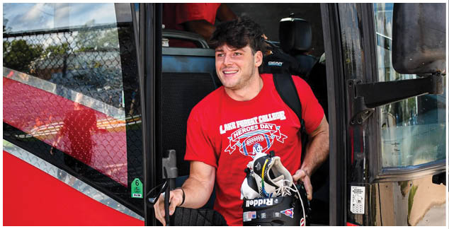 A man wearing a red shirt and black shorts is standing in the doorway of a red bus. Description generated by AI