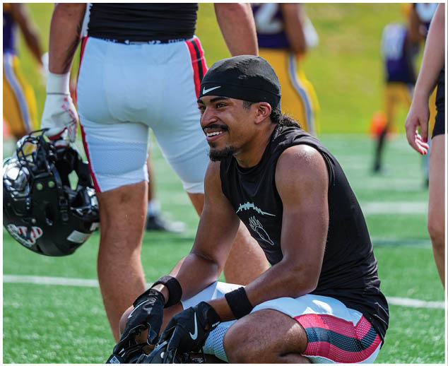 A football player wearing a black helmet and kneeling on the field. Description generated by AI