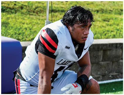 A football player wearing a helmet and kneeling on the field. Description generated by AI
