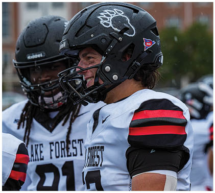 Two football players wearing helmets and jerseys. Description generated by AI