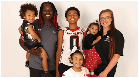 Three adults wearing football jerseys with the number 3 pose smiling against a dark background, with one holding a football. Description generated by AI