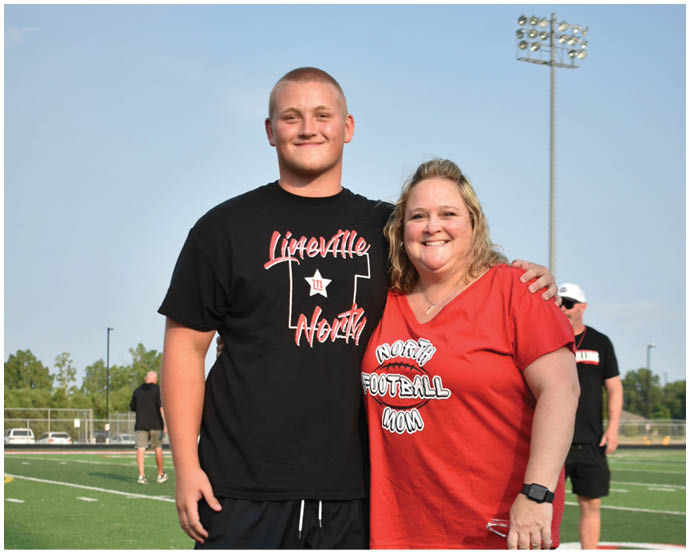 Two adults stand closely together outdoors under a clear sky with a tall stadium light visible in the background. Description generated by AI