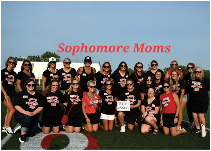 A group of adults wearing matching black and red shirts with “Sophomore Moms" text above them posing outdoors on a sunny day. Description generated by AI