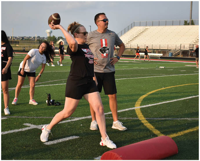 People on a sports field are engaged in a football throwing activity with one person in mid-throw and others watching or stretching nearby. Description generated by AI