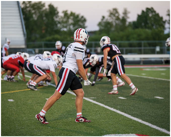 People in football uniforms are positioned on a field preparing for a play during a game. Description generated by AI