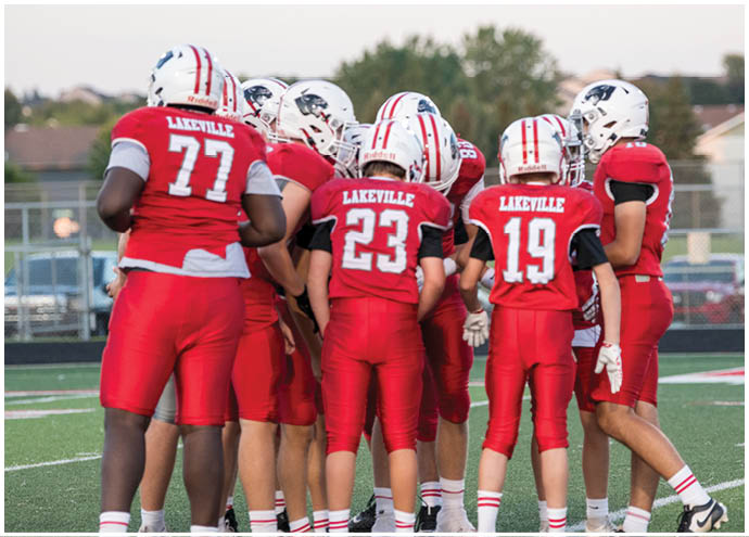 A group of people wearing red football uniforms and helmets are huddled together on a football field during a game or practice. Description generated by AI