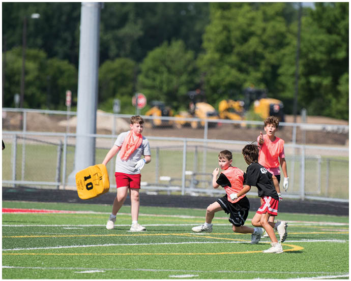 Four children are playing flag football on a field with one child holding a yellow flag and two others running toward each other. Description generated by AI