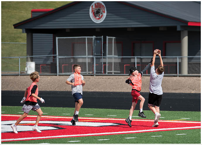 Four children wearing sports clothing are actively playing and jumping on a red and green outdoor sports field. Description generated by AI