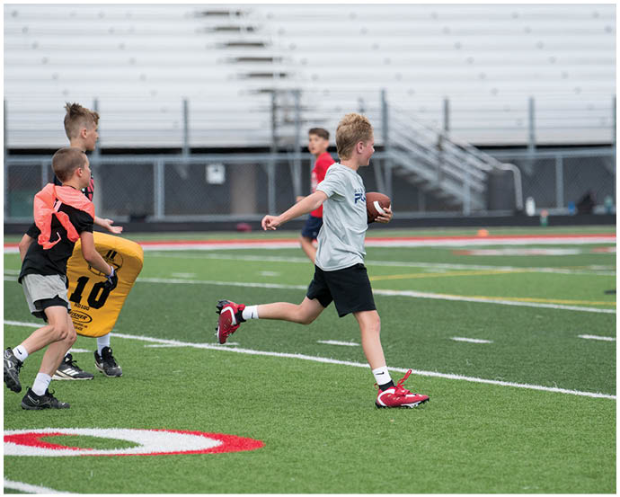 Children playing football on a grassy field with one child running and others nearby. Description generated by AI