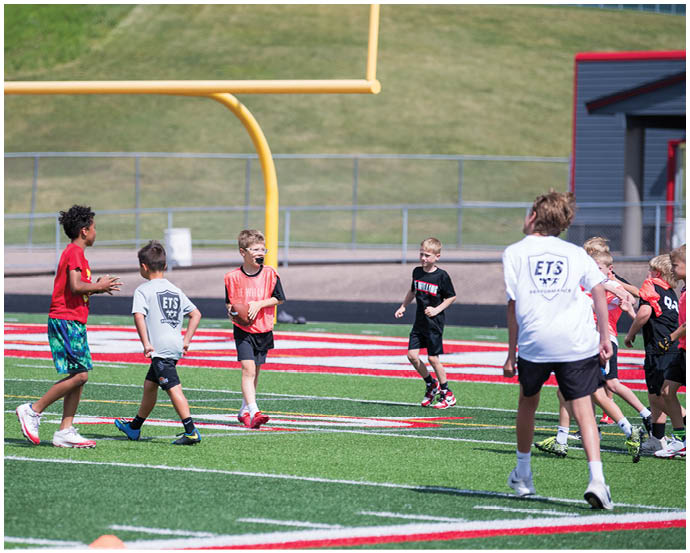 Children wearing sports clothing are playing and running on a football field near a goalpost on a sunny day. Description generated by AI