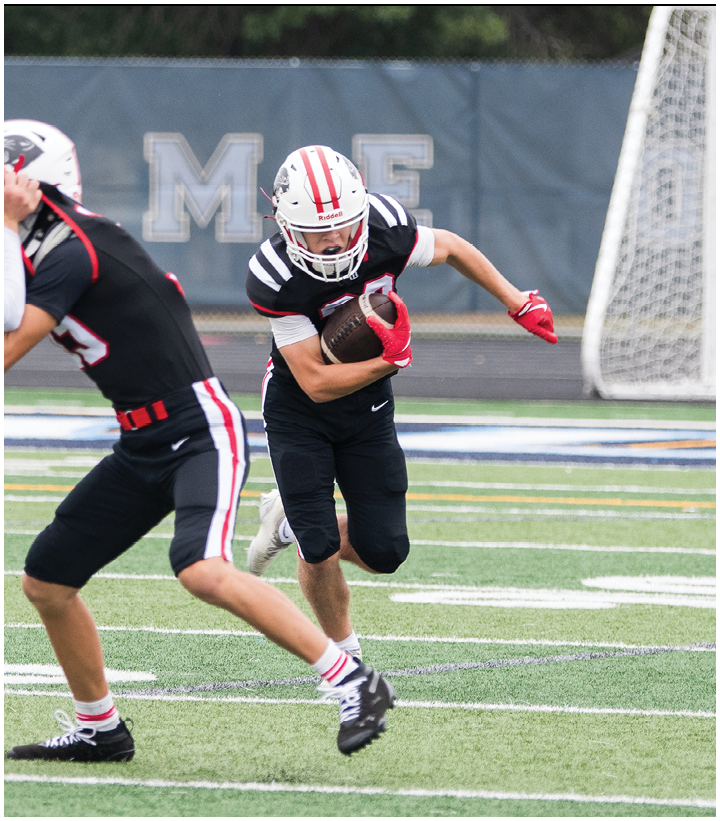 Two people in football uniforms are on a field with one person running while holding a football and the other preparing to throw it. Description generated by AI
