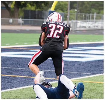 A person wearing a black football uniform with the number 32 and the word Lakeville on the back is standing on a football field near the end zone. Description generated by AI