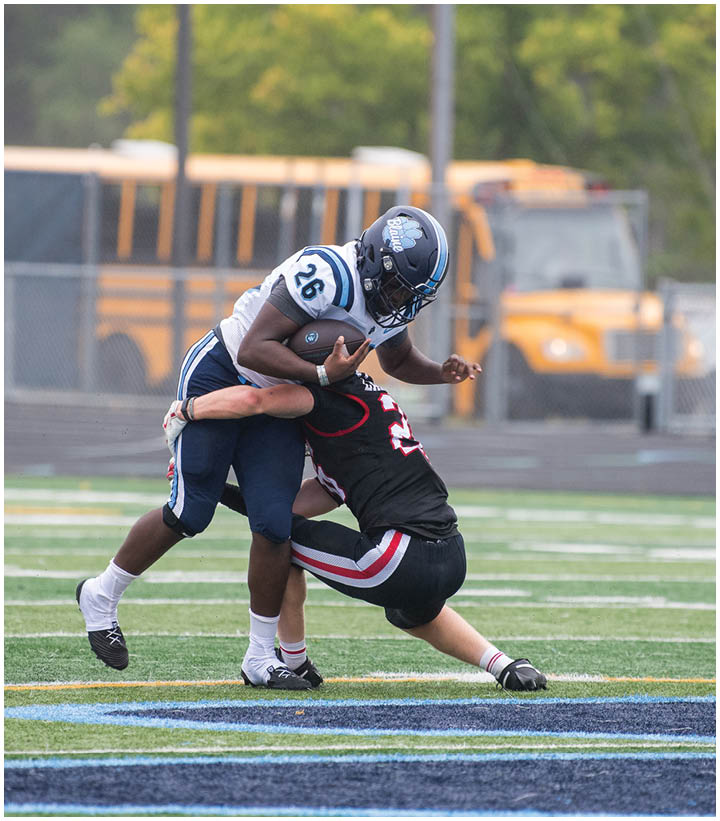 Two people in football uniforms are on a field with one person tackling the other who is holding a football. Description generated by AI