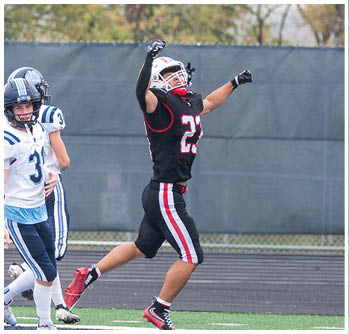 A person in a black and red football uniform is celebrating with arms raised while two people in white and blue football uniforms stand nearby on a field. Description generated by AI