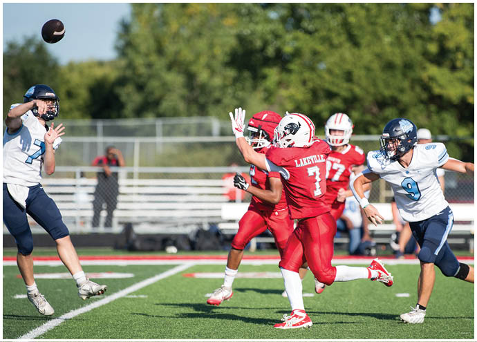 Four people in football uniforms are actively playing on a field with one person throwing a football while others are reaching or running toward it. Description generated by AI