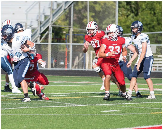 People in football uniforms are actively playing on a field with one person running while holding the ball and others in pursuit. Description generated by AI