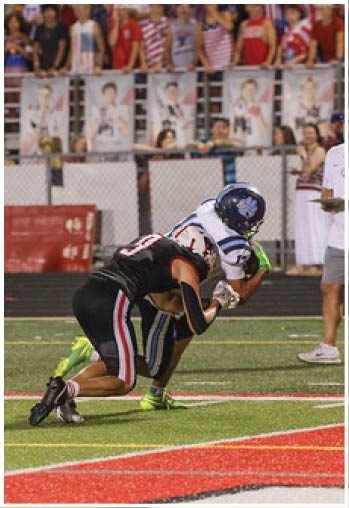 Two people in football uniforms are on a field near the end zone with spectators and banners in the background. Description generated by AI