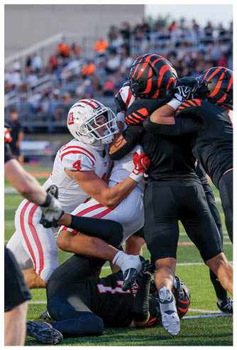 A person in a white football uniform with the number 4 is tackling another person in a black football uniform during a game. Description generated by AI
