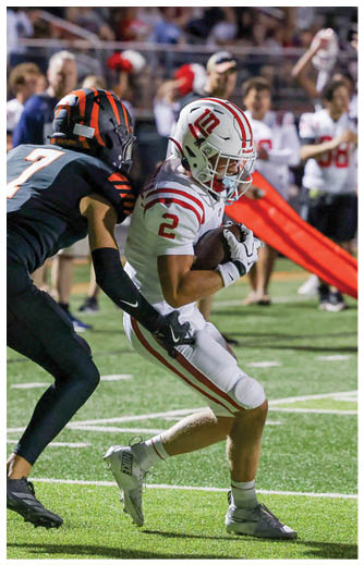 Two people in white football uniforms are near the end zone with one person in a black uniform attempting to tackle the player holding the ball. Description generated by AI