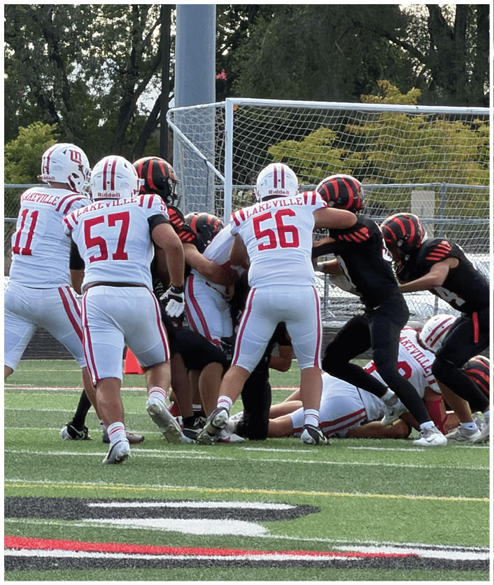 A group of people wearing football uniforms from two different teams are engaged in a play near the goalpost on a football field. Description generated by AI