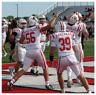 People in white football uniforms celebrating on a field with others in black uniforms and spectators in the background. Description generated by AI