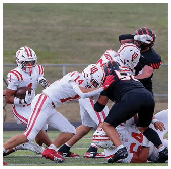 A group of football players in white and black uniforms are engaged in a play on a grassy field with one player holding the ball and others blocking or tackling. Description generated by AI