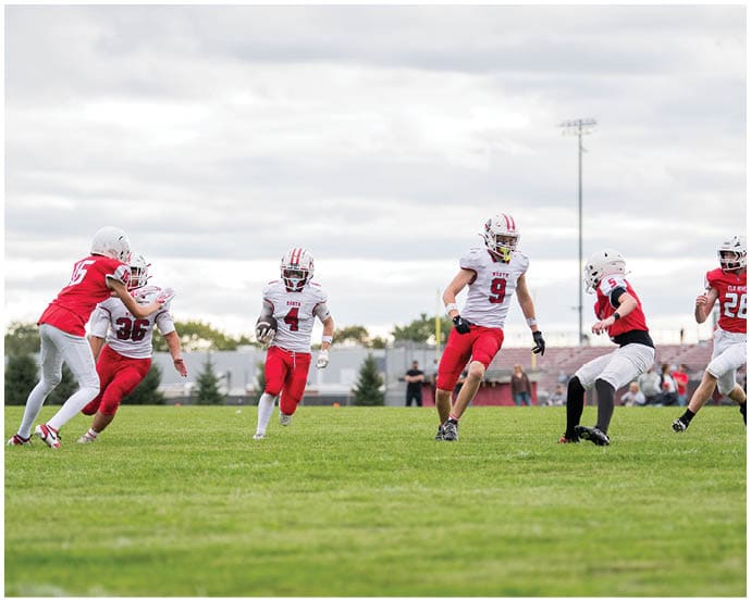 Three people in football uniforms are running on a grassy field during a game with a cloudy sky in the background. Description generated by AI