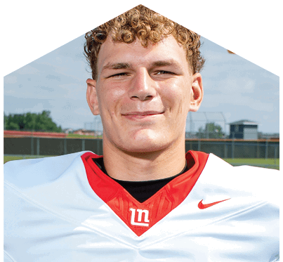 A person with curly hair is smiling and wearing a white and red football jersey with a black undershirt, standing outdoors on a sports field. Description generated by AI