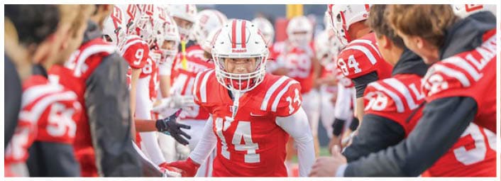 A person in a red and white football uniform with the number 14 is walking through a line of teammates who are reaching out to give high-fives. Description generated by AI