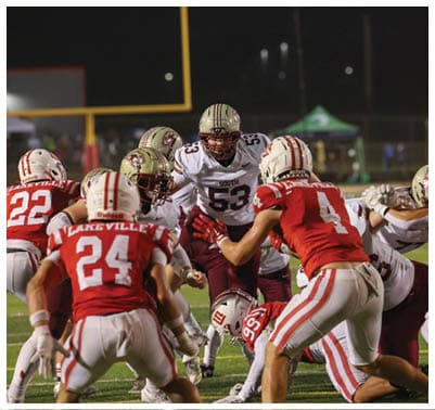 Several football players in helmets and uniforms are engaged in a play on a field during a game at night. Description generated by AI
