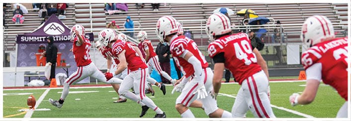 Several people wearing red and white sports uniforms are running on a green field, likely participating in a football game or practice. Description generated by AI