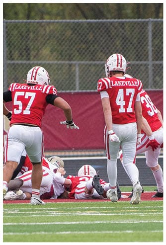 Several people in red and white football uniforms are on a field with some lying on the ground and others standing, with one person raising their arms in celebration. Description generated by AI