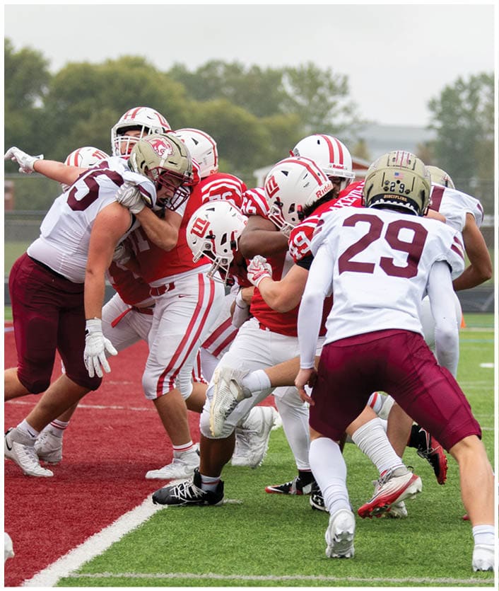 A group of people wearing football uniforms are actively engaged in a play on a football field near the end zone. Description generated by AI