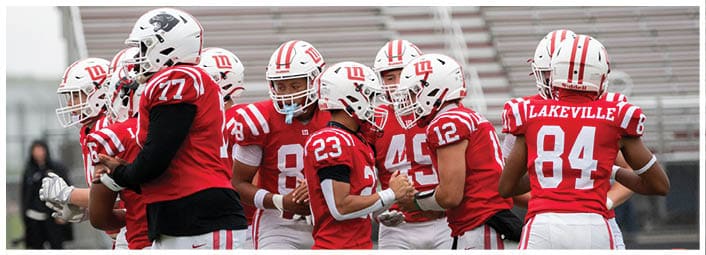A group of people wearing red and white football uniforms are standing together on a green field. Description generated by AI