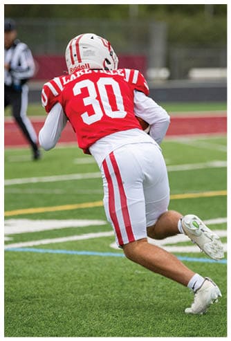 A person wearing a red and white football uniform with the number 30 is running on a grassy field. Description generated by AI
