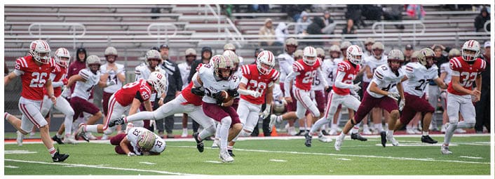 A group of people in football uniforms are actively playing on a field with one person running while holding the ball and others chasing or attempting to tackle. Description generated by AI