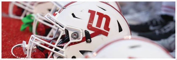 A row of white football helmets with red logos is lined up on a red turf field. Description generated by AI