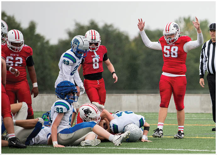 People in football uniforms are on a field with one person lying on the ground and others standing nearby. Description generated by AI