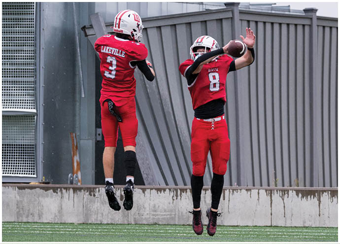 Two people in red football uniforms are jumping on a field, with one catching a football. Description generated by AI