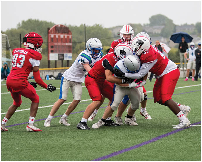 Several people in football uniforms are engaged in a tackle on a grassy field during a game. Description generated by AI