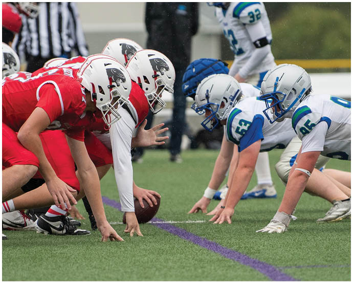 Two opposing youth football teams in red and white uniforms are lined up on the field facing each other, ready for the play to begin. Description generated by AI