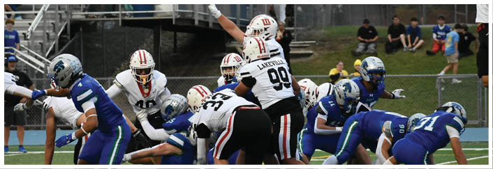 A group of people in football uniforms are actively engaged in a play on a football field with some players tackling and others running. Description generated by AI