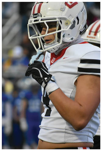 A person wearing a white football uniform and helmet is adjusting their chin strap on the field during a game. Description generated by AI