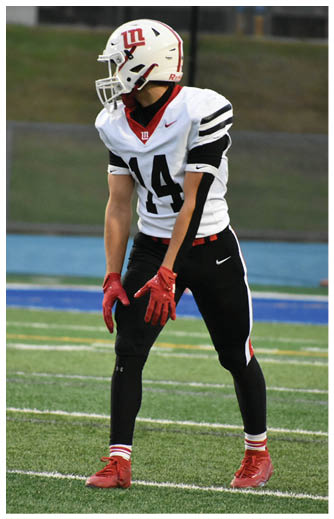 A person wearing a white football helmet, white jersey with the number 14, black pants, red gloves, and red cleats is standing on a football field in a ready position. Description generated by AI