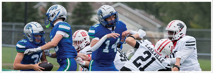 People in football uniforms are actively engaged in a game on a field with a fence and trees in the background. Description generated by AI