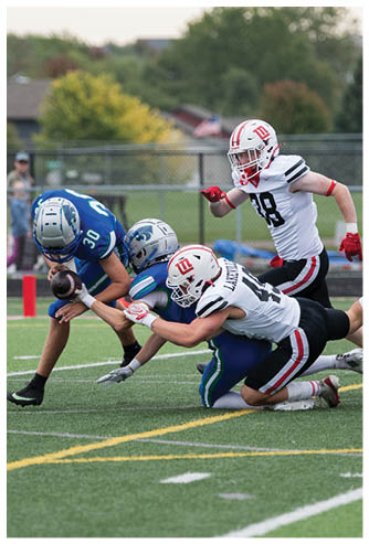 Two people in football uniforms are engaged in a tackle on a grassy field during a game. Description generated by AI