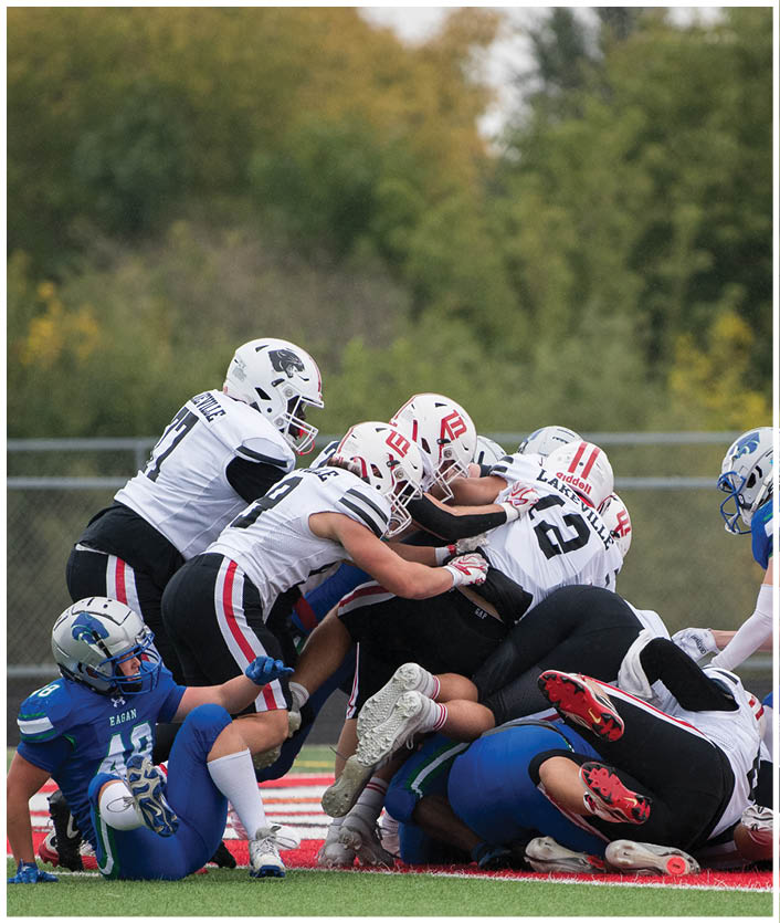 Several people in football uniforms are engaged in a tackle on a field with a blurred green background. Description generated by AI